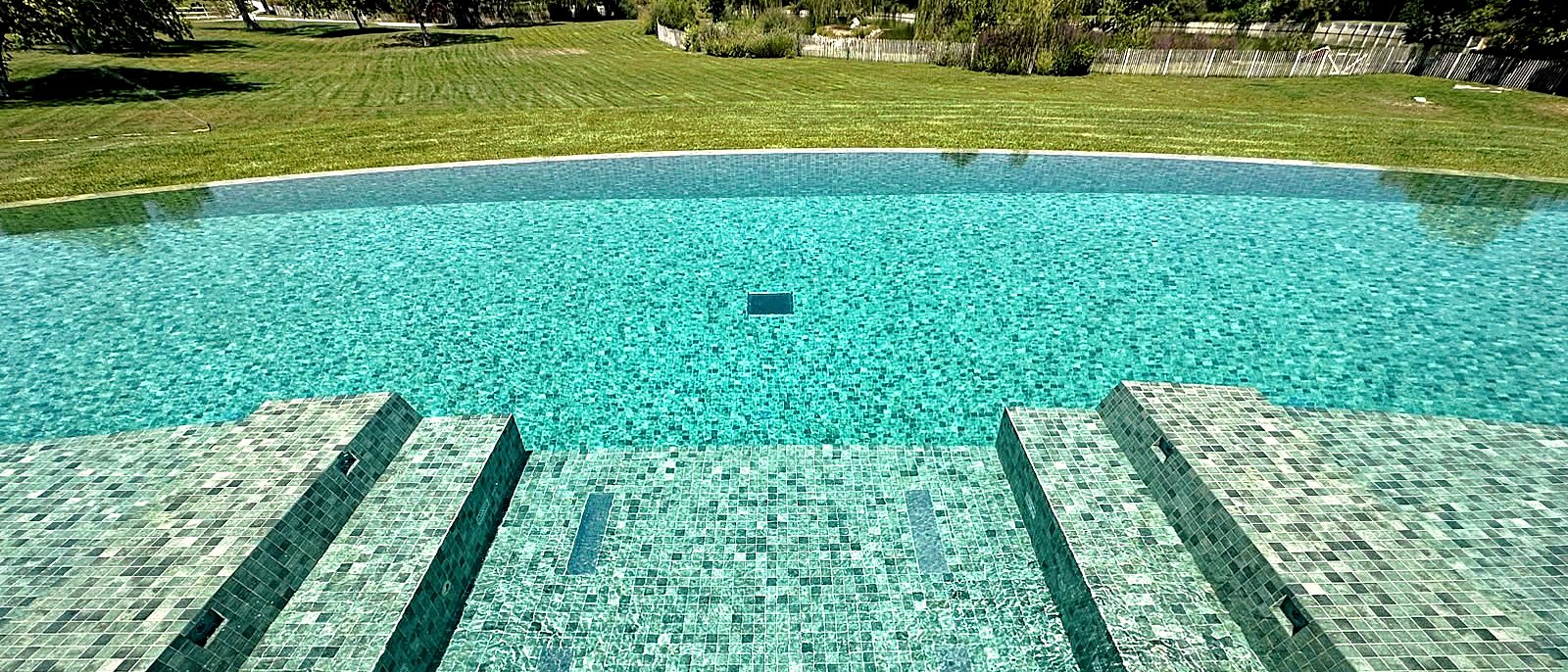 Escalier d'accès en mosaïque d'une piscine face à un parc